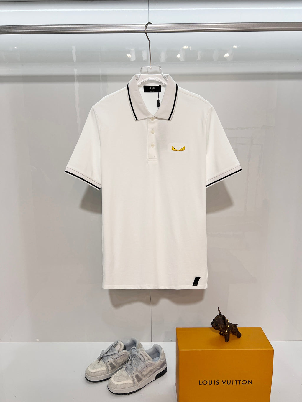 A polo shirt with embroidered letters on the eyes of a golden little monster on the chest