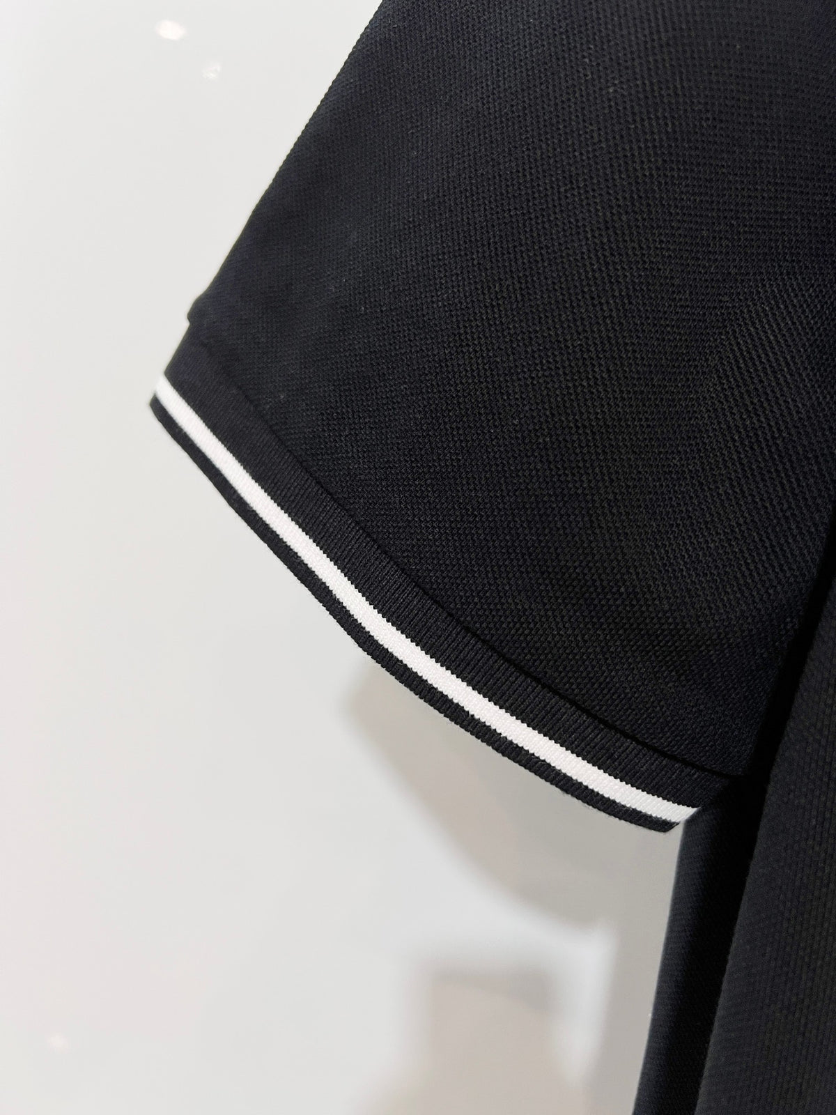 A polo shirt with embroidered letters on the eyes of a golden little monster on the chest