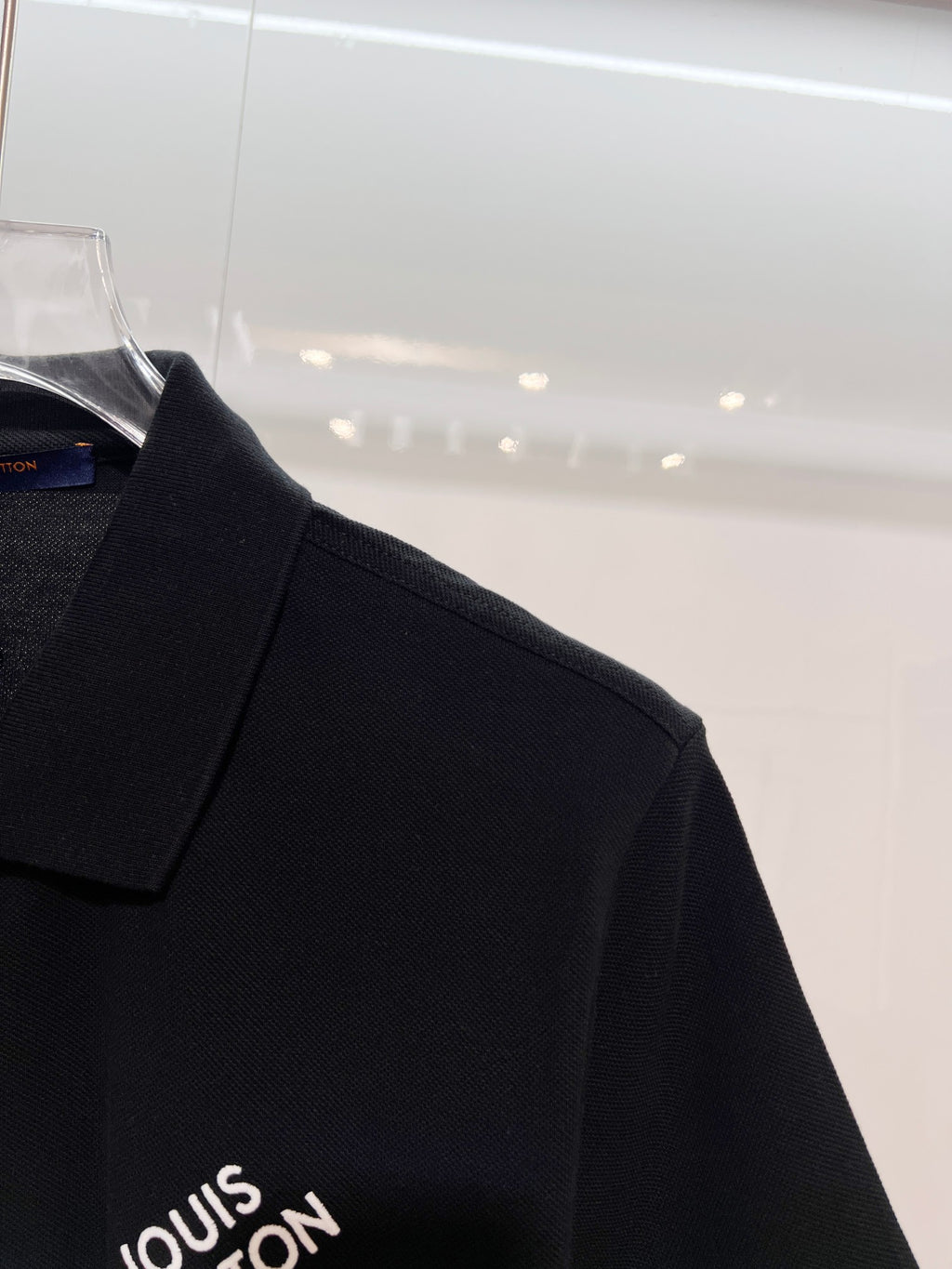 A polo shirt with embroidered letters on the eyes of a golden little monster on the chest