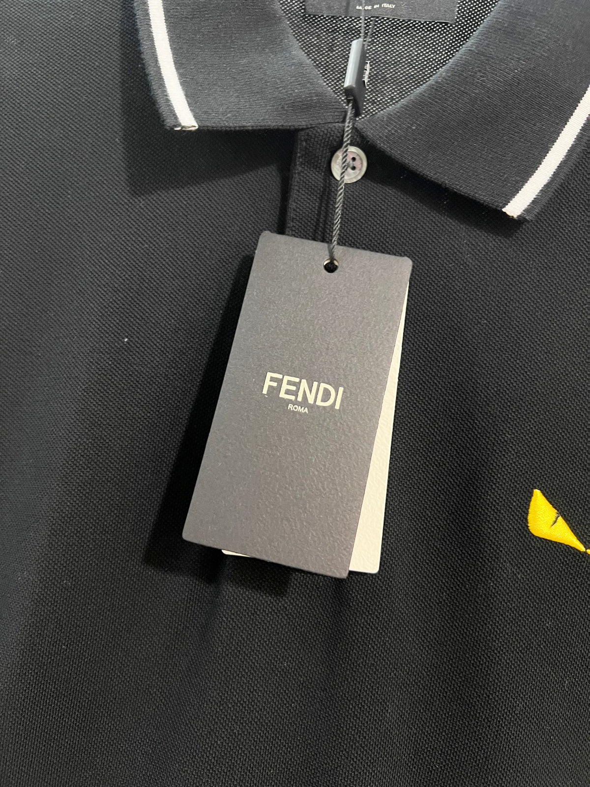 A polo shirt with embroidered letters on the eyes of a golden little monster on the chest
