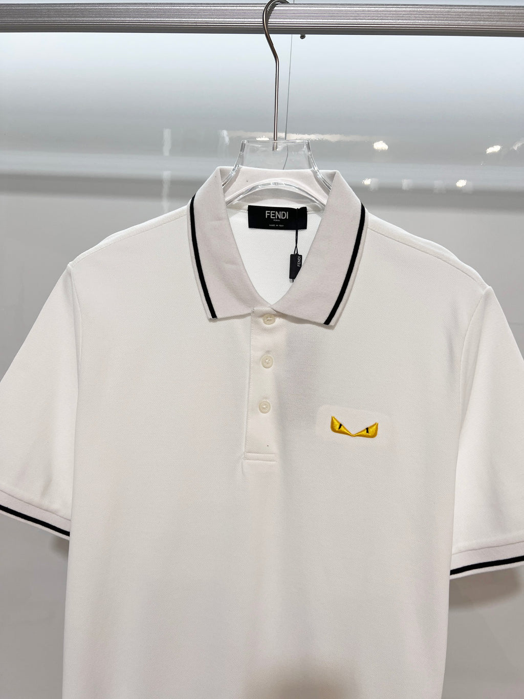 A polo shirt with embroidered letters on the eyes of a golden little monster on the chest