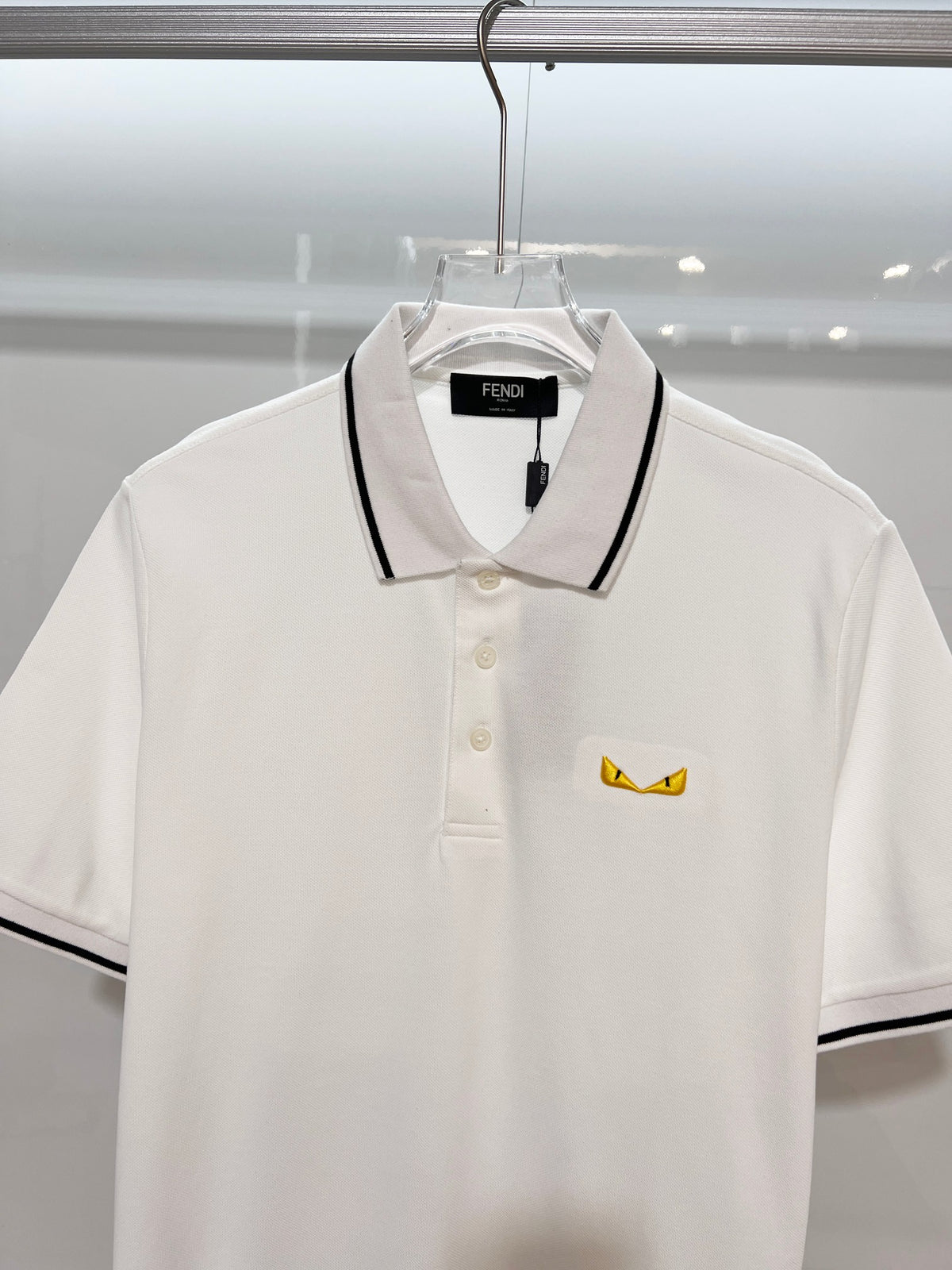 A polo shirt with embroidered letters on the eyes of a golden little monster on the chest