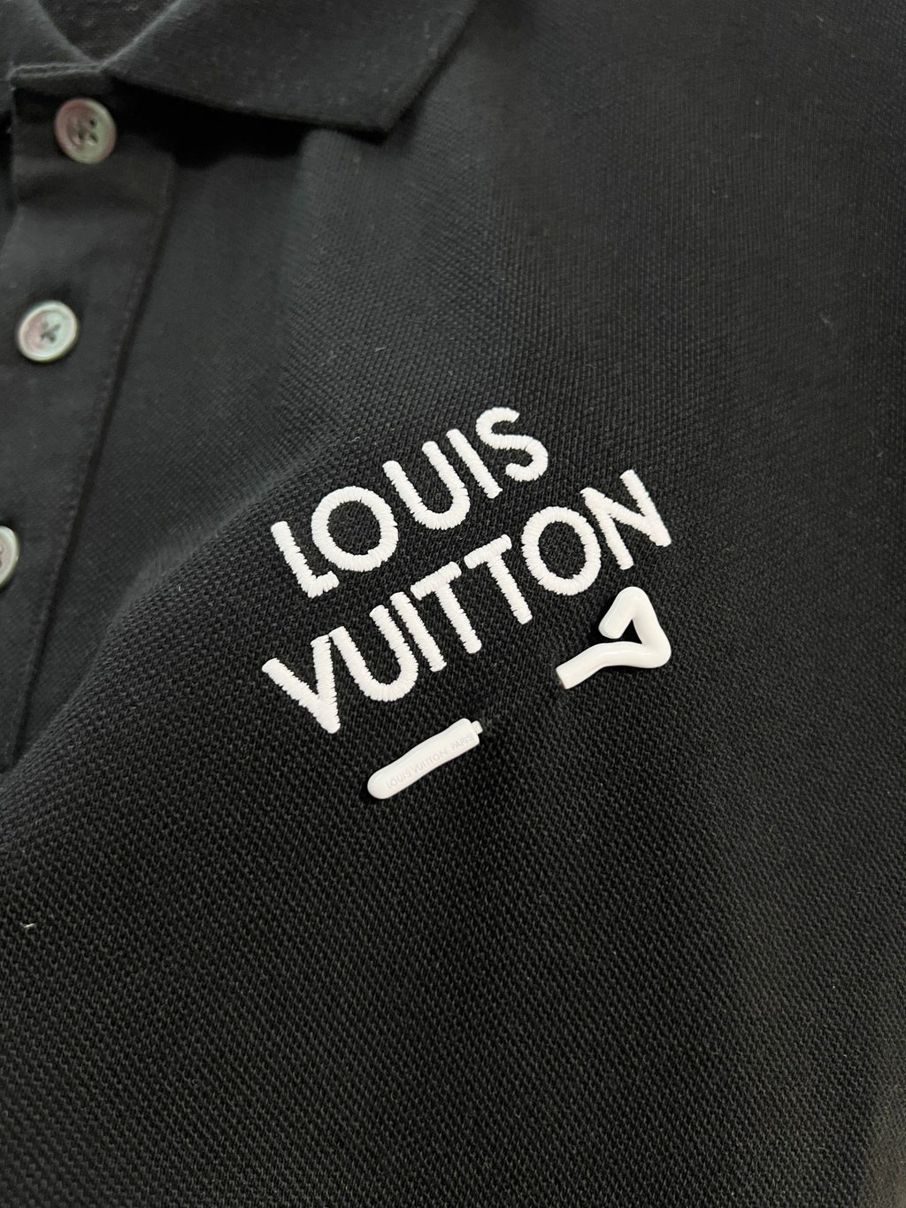 A polo shirt with embroidered letters on the eyes of a golden little monster on the chest