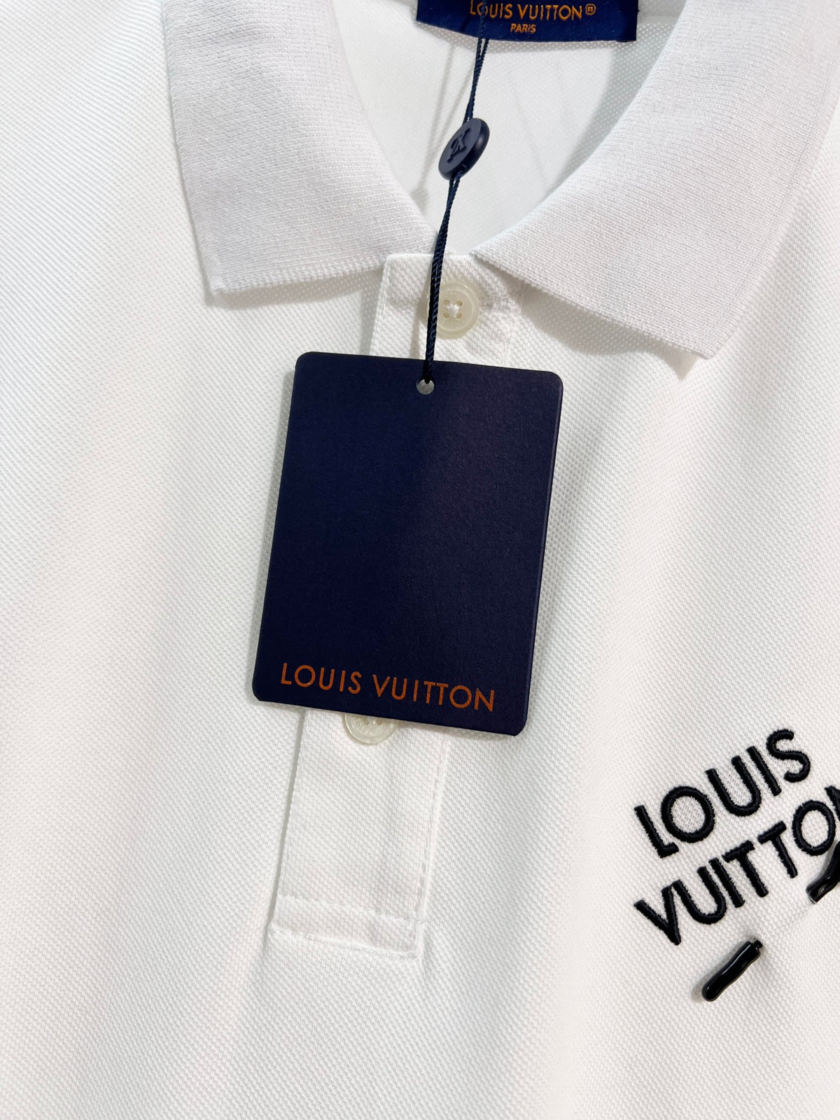 A polo shirt with embroidered letters on the eyes of a golden little monster on the chest