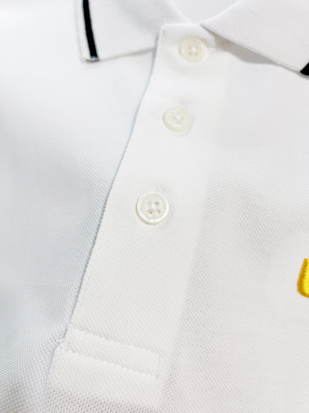 A polo shirt with embroidered letters on the eyes of a golden little monster on the chest