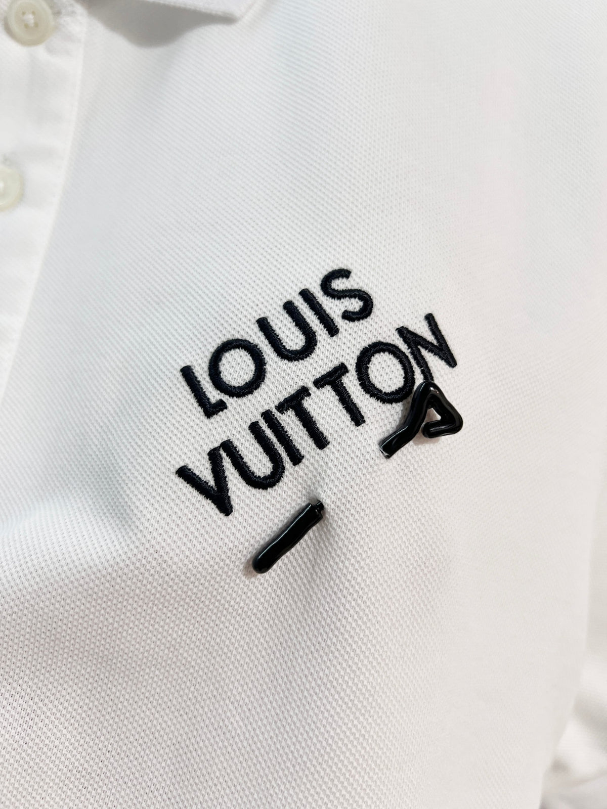 A polo shirt with embroidered letters on the eyes of a golden little monster on the chest