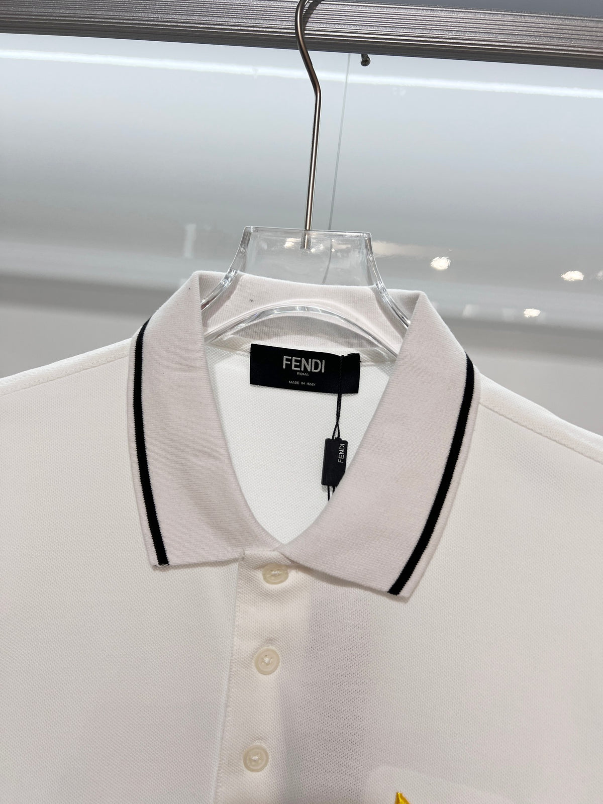 A polo shirt with embroidered letters on the eyes of a golden little monster on the chest