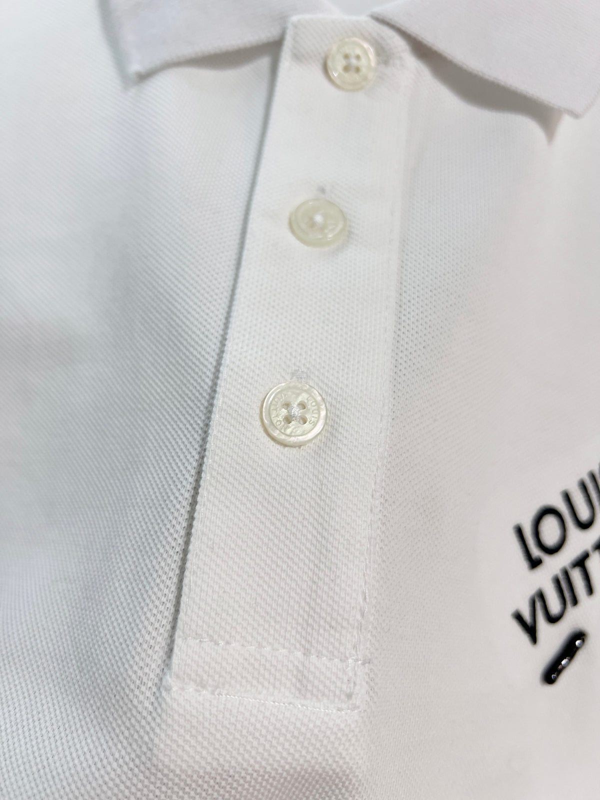 A polo shirt with embroidered letters on the eyes of a golden little monster on the chest