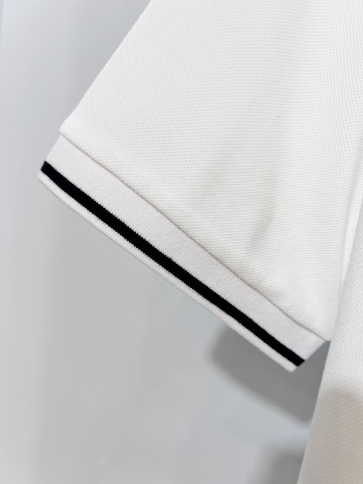 A polo shirt with embroidered letters on the eyes of a golden little monster on the chest