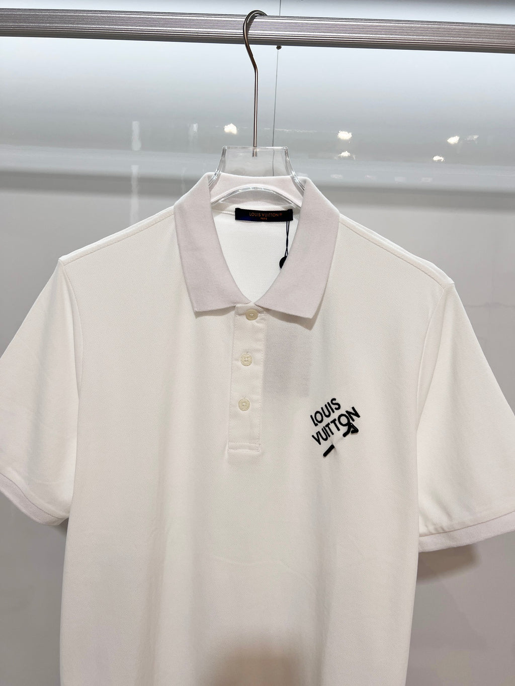 A polo shirt with embroidered letters on the eyes of a golden little monster on the chest