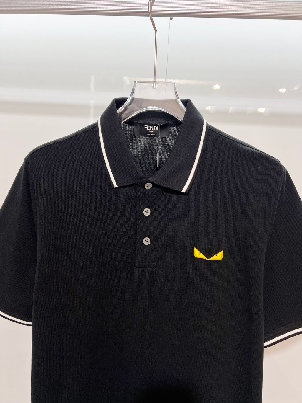 A polo shirt with embroidered letters on the eyes of a golden little monster on the chest