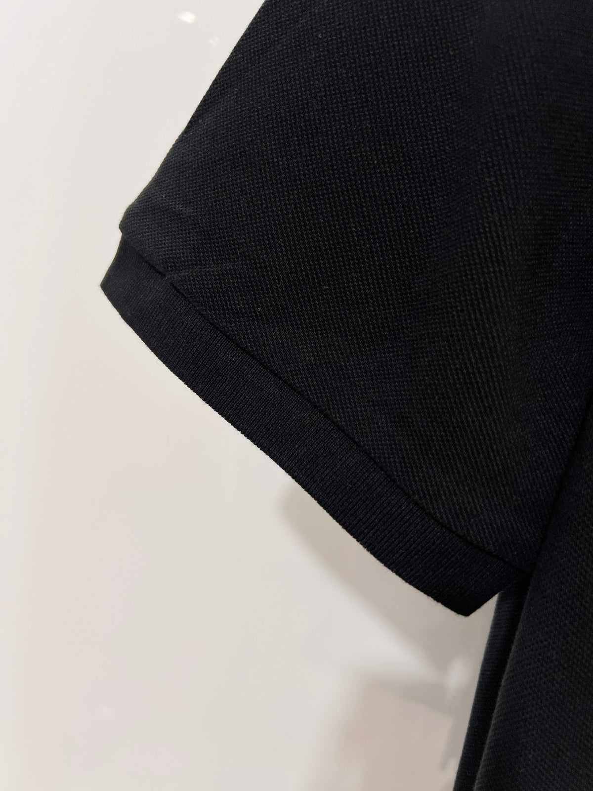 A polo shirt with embroidered letters on the eyes of a golden little monster on the chest