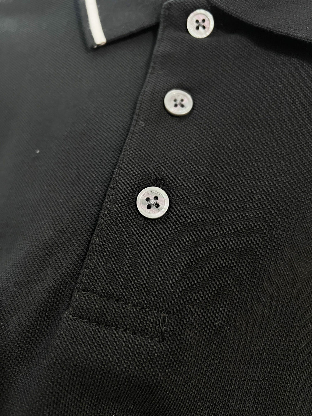 A polo shirt with embroidered letters on the eyes of a golden little monster on the chest