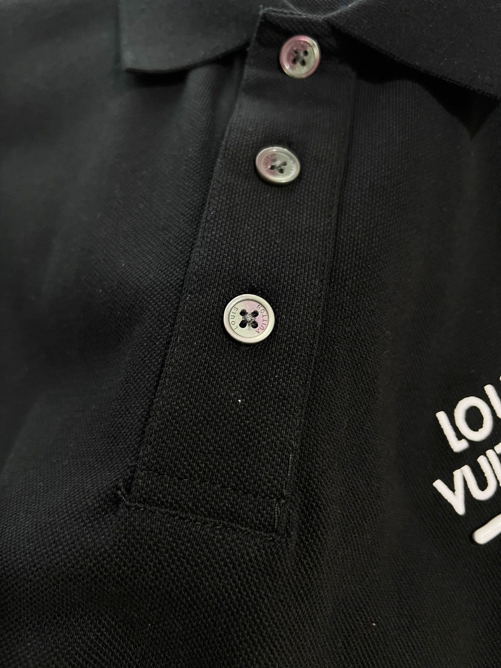 A polo shirt with embroidered letters on the eyes of a golden little monster on the chest