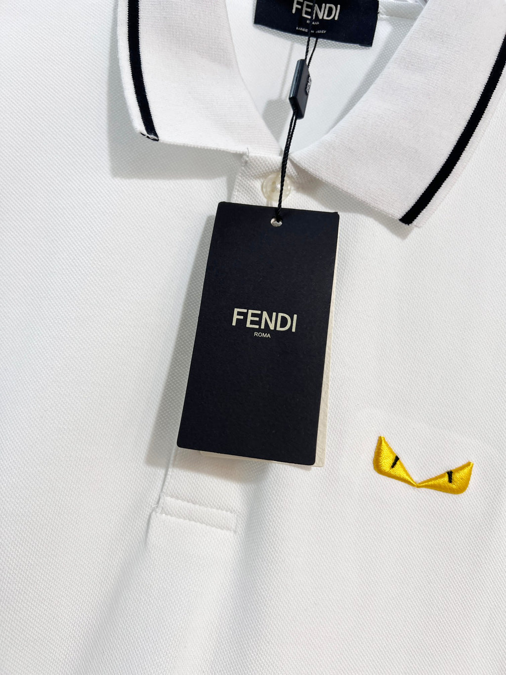 A polo shirt with embroidered letters on the eyes of a golden little monster on the chest