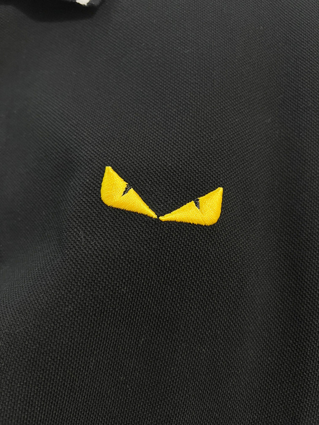 A polo shirt with embroidered letters on the eyes of a golden little monster on the chest