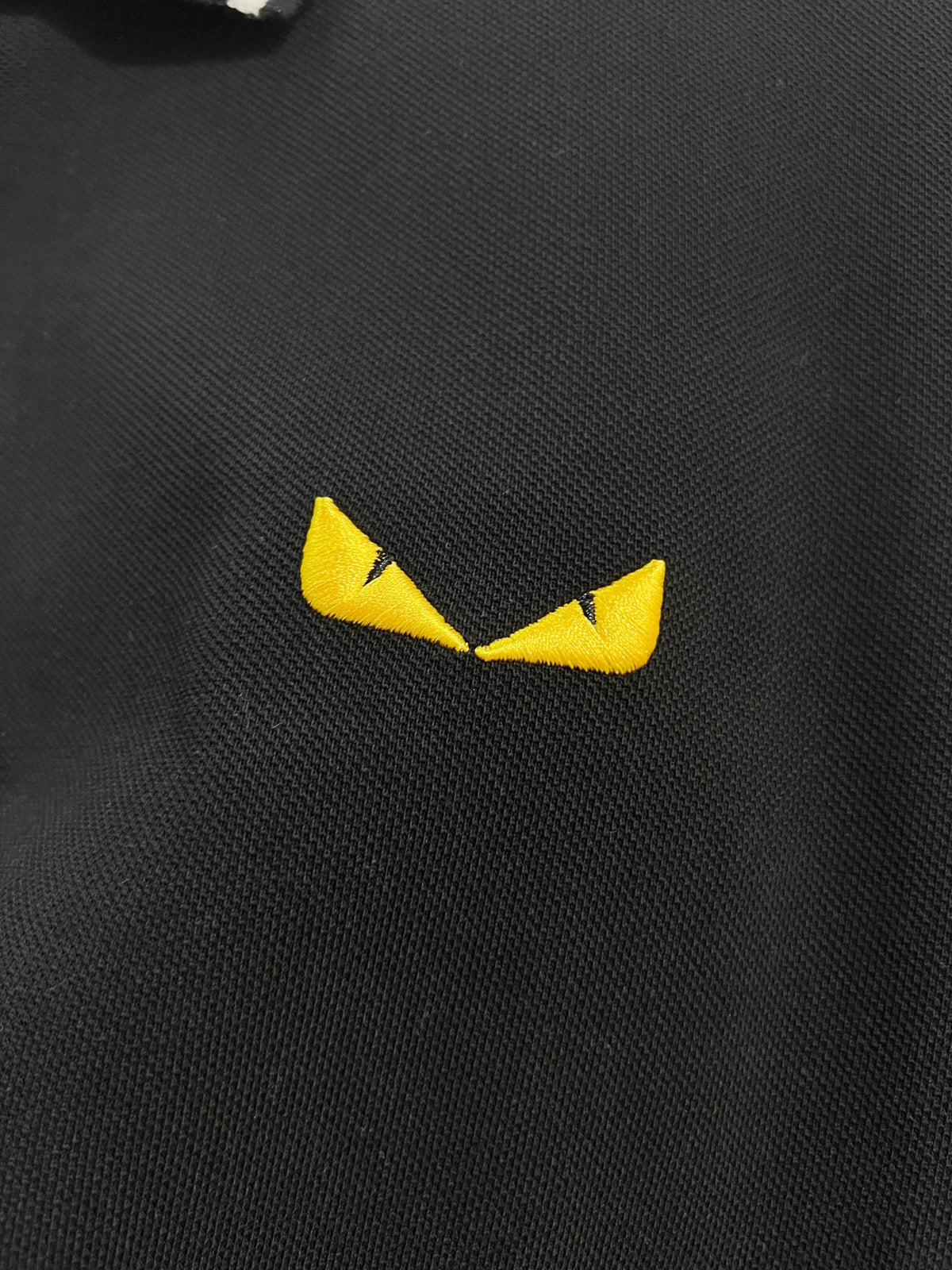 A polo shirt with embroidered letters on the eyes of a golden little monster on the chest