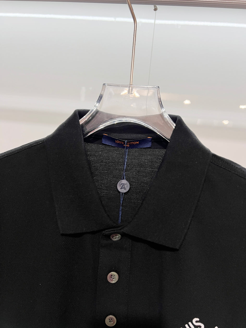 A polo shirt with embroidered letters on the eyes of a golden little monster on the chest