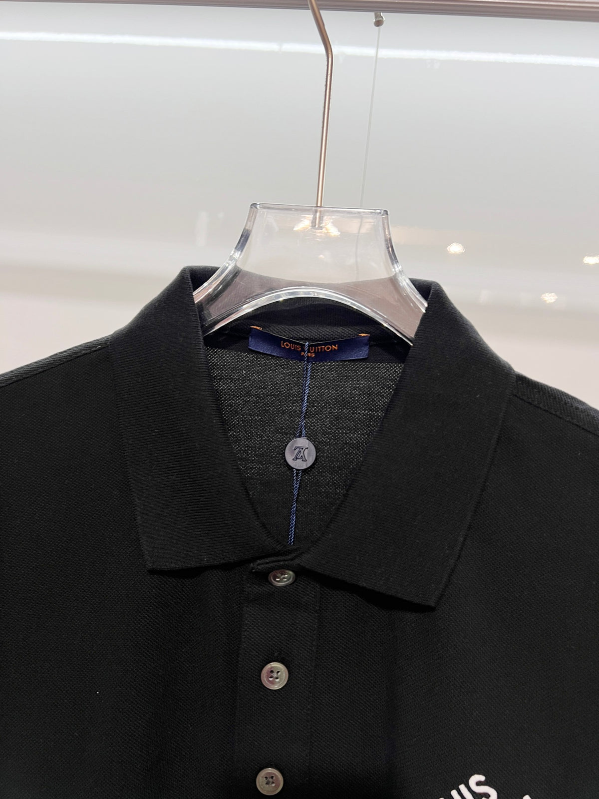 A polo shirt with embroidered letters on the eyes of a golden little monster on the chest