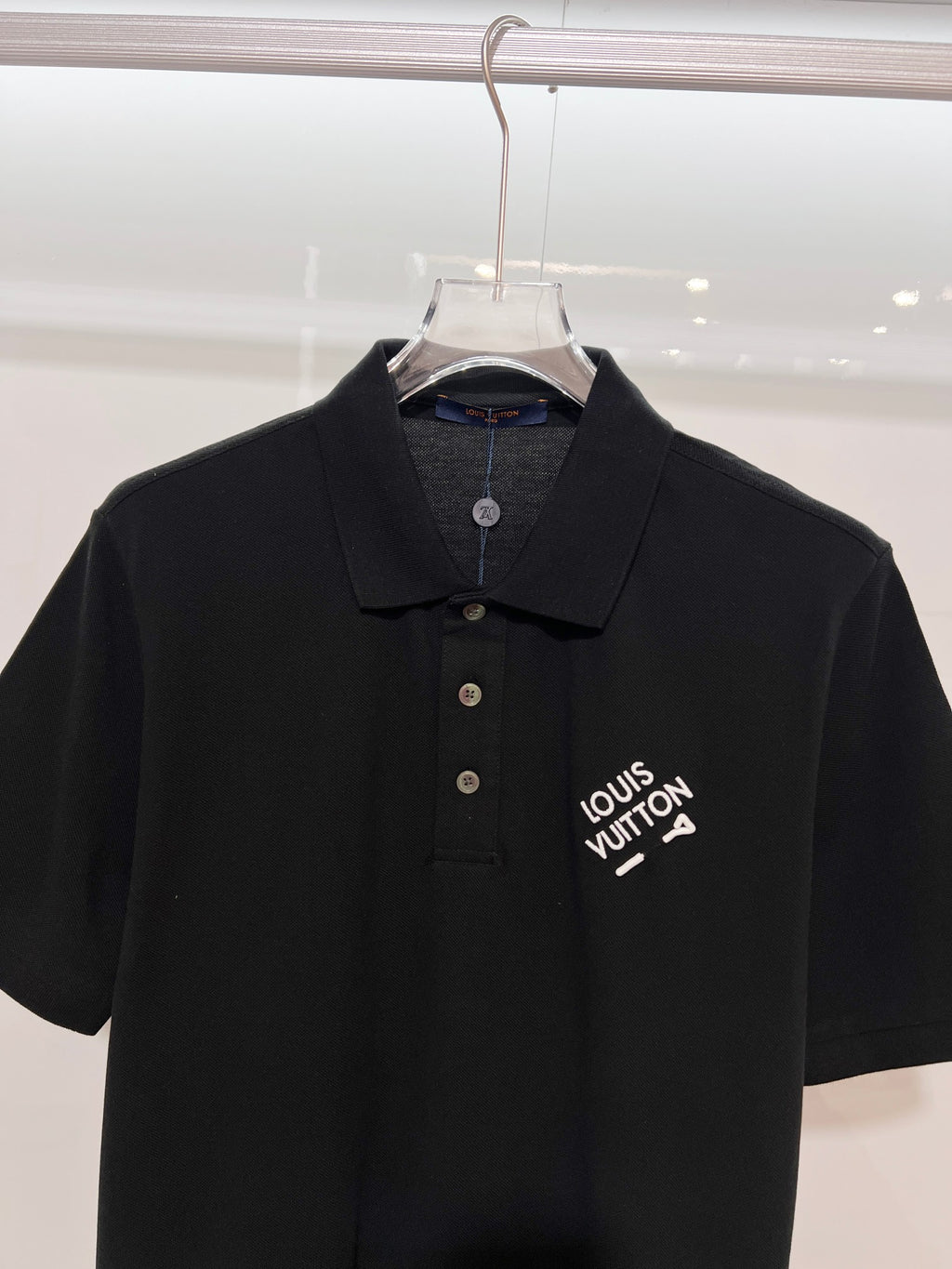 A polo shirt with embroidered letters on the eyes of a golden little monster on the chest