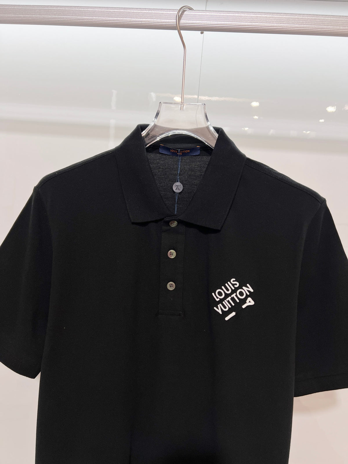 A polo shirt with embroidered letters on the eyes of a golden little monster on the chest