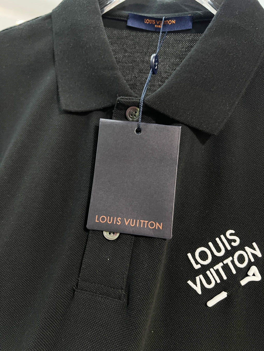A polo shirt with embroidered letters on the eyes of a golden little monster on the chest
